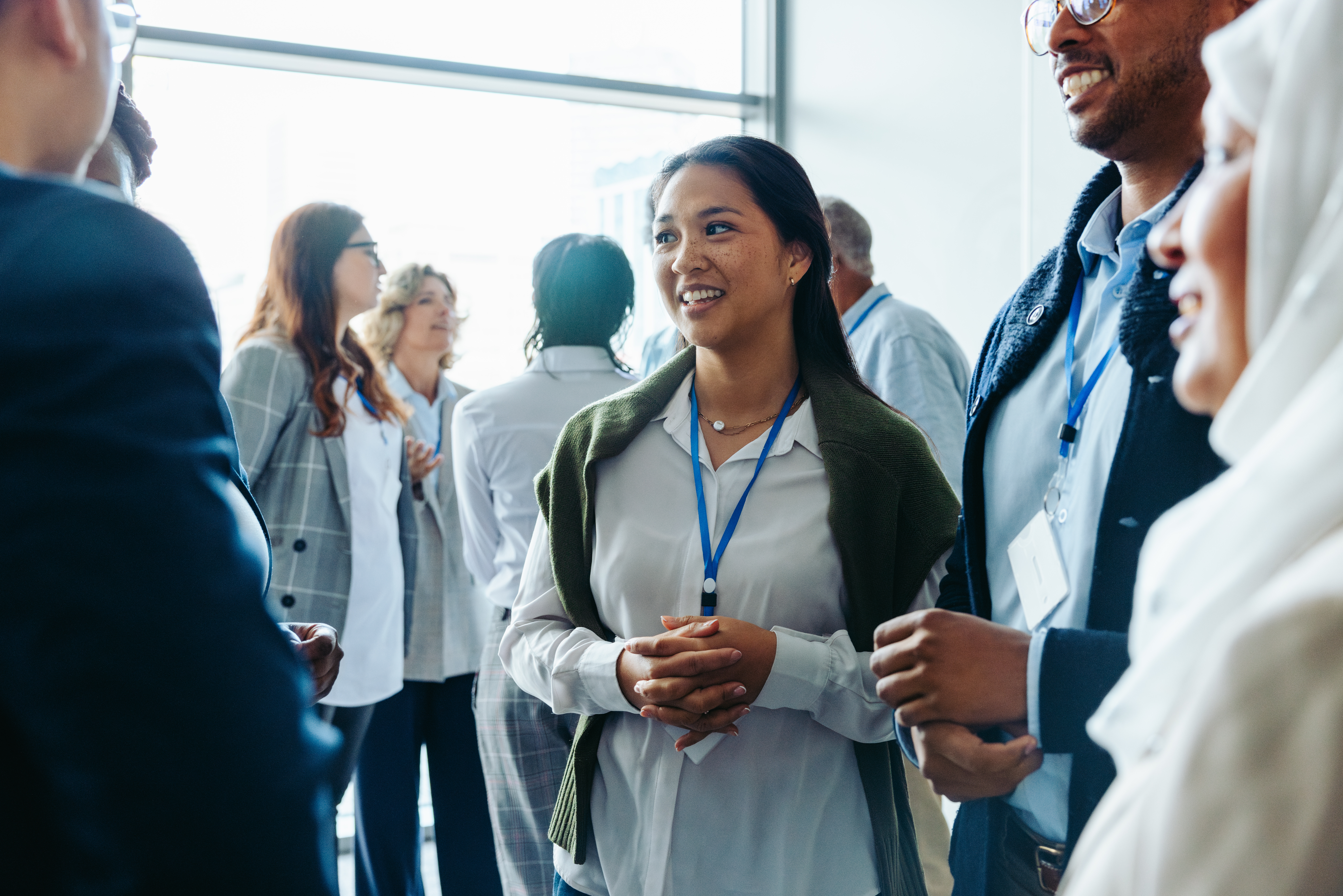 Group of diverse business professionals, businessmen and businesswomen, networking at a conference event. They are smiling, conversing, and engaging in discussions during a daytime seminar.