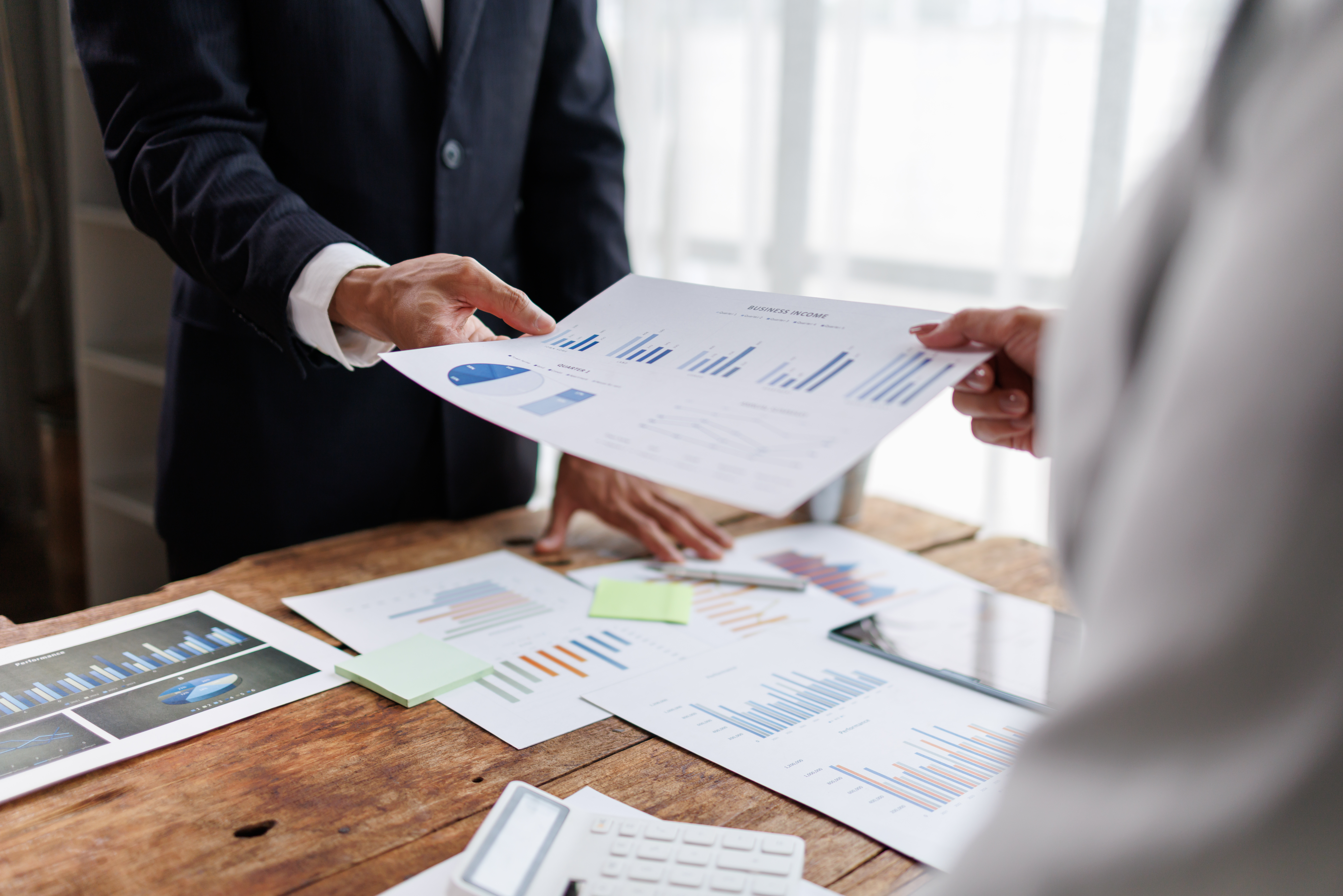Business people collaborating on financial analysis, exchanging documents with market data reports, charts, and graphs during a corporate meeting in an office environment